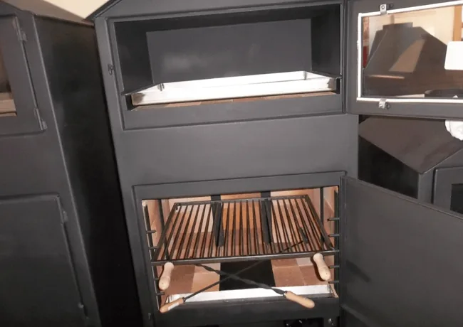Barbacoa negra con horno arriba y parrilla con asadores abajo, con las puertas abiertas en una exposición