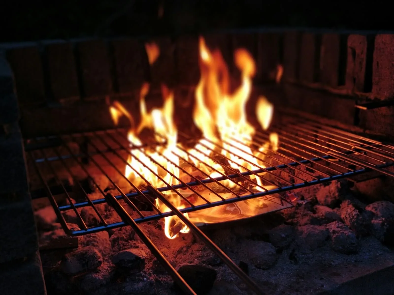 Llamas que suben entre las varillas de la parrilla de una barbacoa de ladrillo, sobre las brasas, de noche